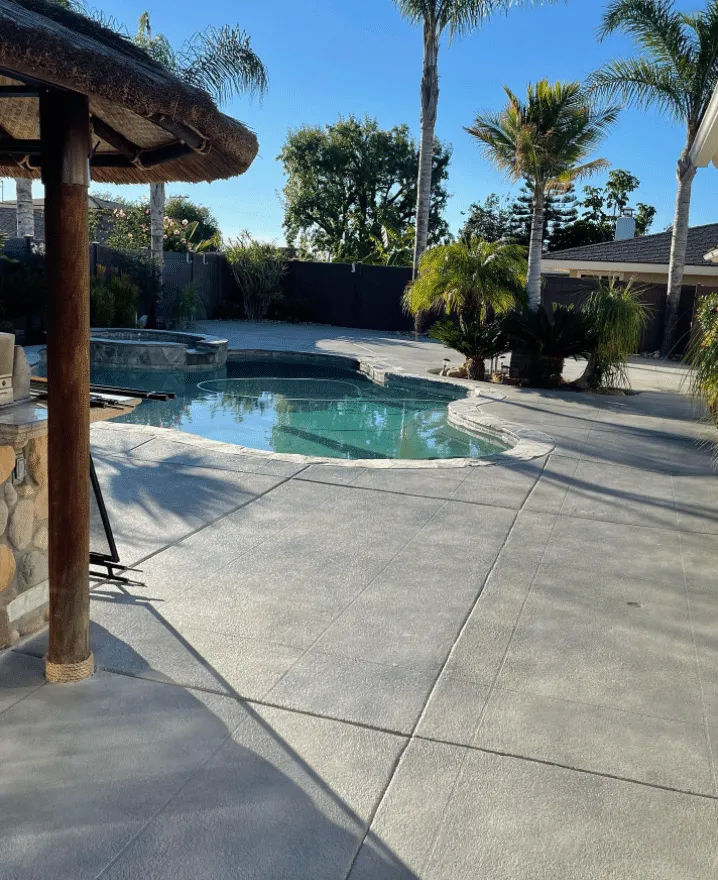 Concrete pool deck beside a backyard pool