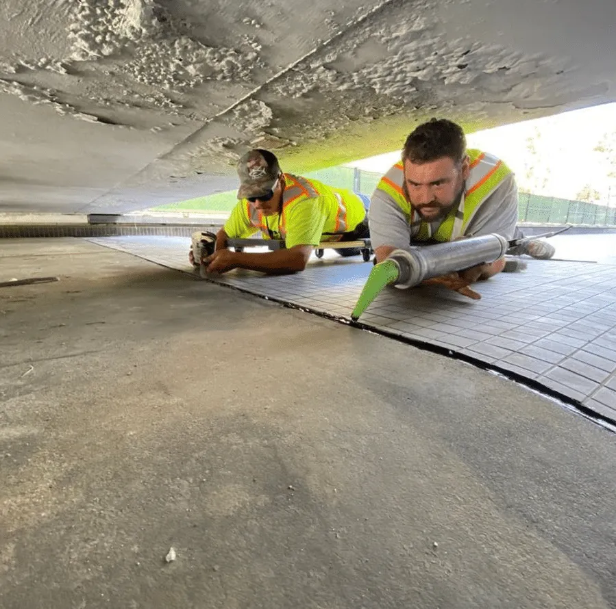 Two crew members caulking a concrete joint