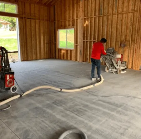 Worker grinding concrete in a wood-framed room
